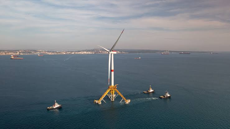 Industrial floating wind turbine at sea with tugboats